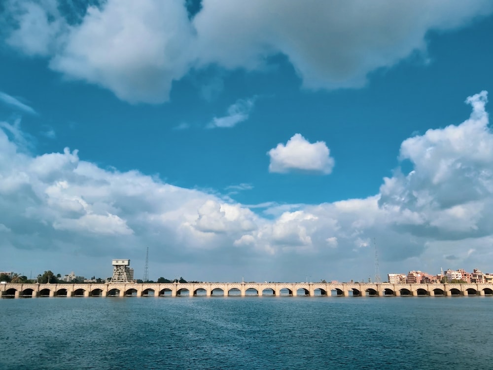 ponte di cemento bianco sopra lo specchio d'acqua sotto il cielo blu e le nuvole bianche durante il giorno