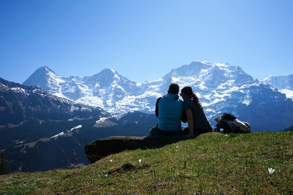 낮에 눈 덮인 산 근처의 바위에 앉아 있는 남자와 여자