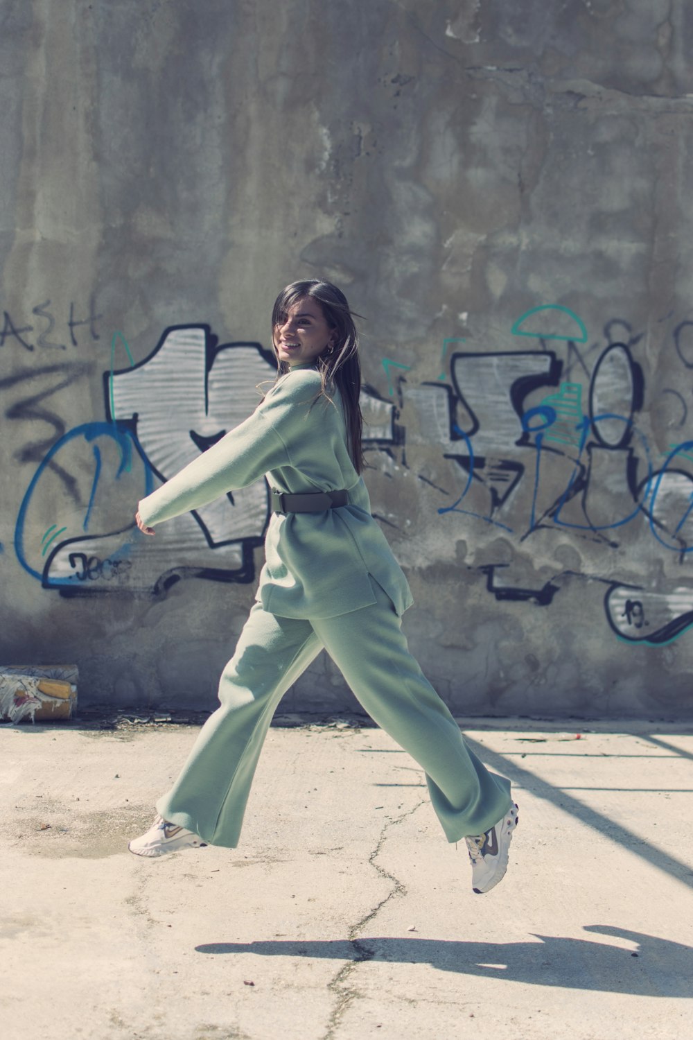 woman in green long sleeve shirt and pants standing beside graffiti wall during daytime