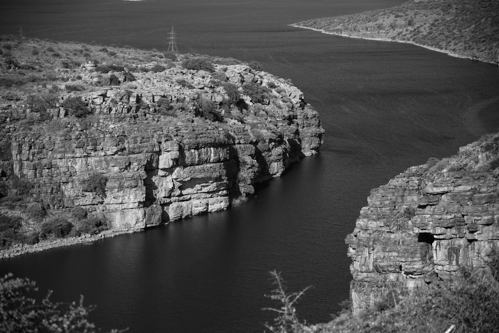 grayscale photo of person standing on rock formation near body of water