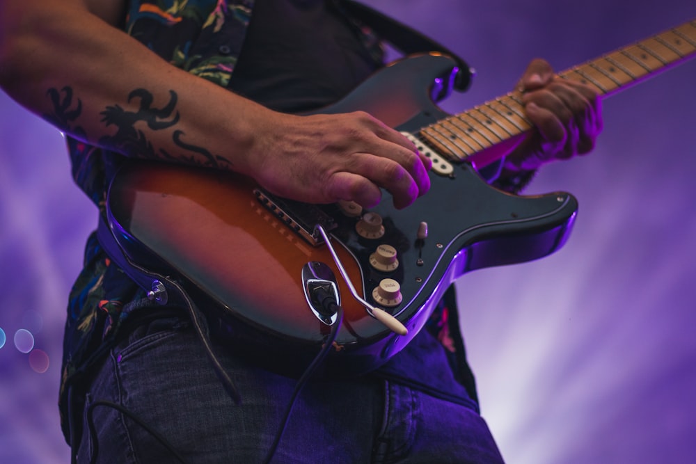 갈색과 흰색 스트라토캐스터 일렉트릭 기타를 연주하는 검은색 티셔츠를 입은 남자