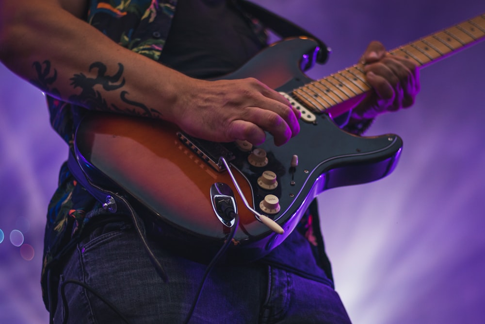 man in black t-shirt playing brown and white stratocaster electric guitar