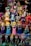 A collection of colorful figurines displayed on shelves, featuring various characters in different costumes including princesses, superheroes, and zombies. The figurines are made in a playful, cartoonish style.