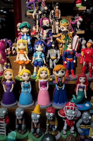 A collection of colorful figurines displayed on shelves, featuring various characters in different costumes including princesses, superheroes, and zombies. The figurines are made in a playful, cartoonish style.