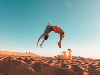 man in blue shirt and brown shorts jumping on brown sand during daytime