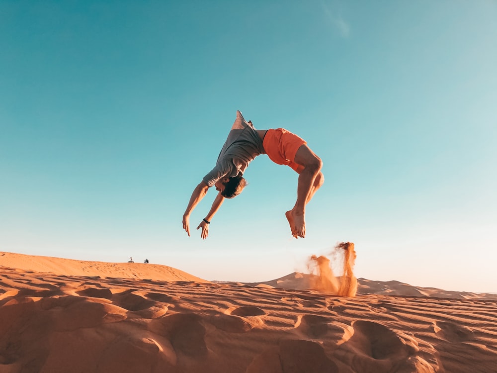 homme en chemise bleue et short marron sautant sur le sable brun pendant la journée