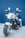 A small, sleek electric toy motorcycle with shiny chrome details and a black and white color scheme. The motorcycle has two rear-view mirrors, red lights, and a wide front tire, positioned in front of a blue background.