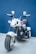 A small, sleek electric toy motorcycle with shiny chrome details and a black and white color scheme. The motorcycle has two rear-view mirrors, red lights, and a wide front tire, positioned in front of a blue background.