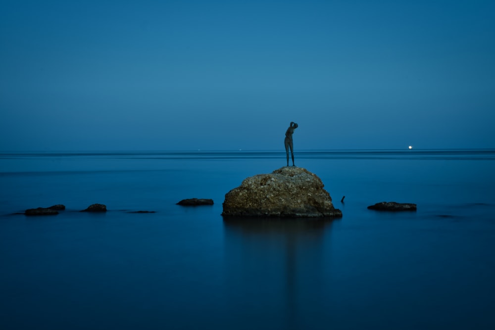 man standing on rock in the middle of the sea