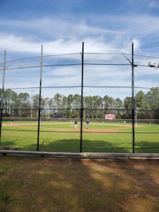 Cricket players practicing on a turf net with coaches guiding them during a sunny day.