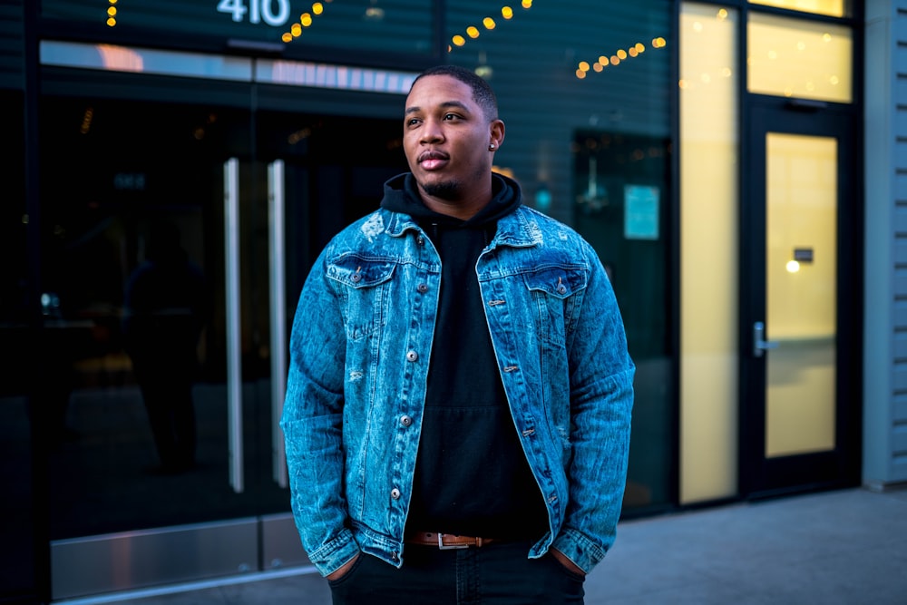 man in blue denim jacket standing near glass window during daytime