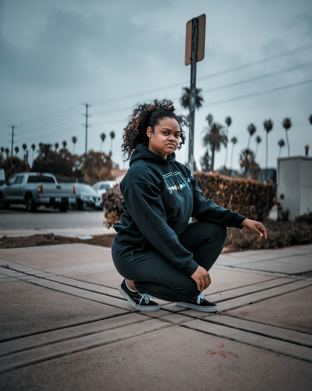 woman in black hoodie and blue pants sitting on brown wooden floor during daytime