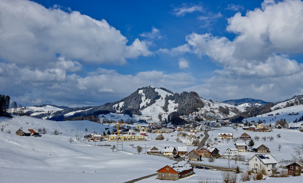 white and brown houses near snow covered mountain under blue and white cloudy sky during daytime