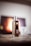 A sleek, metallic vape device stands on a table with a warm, blurred background. The device has a transparent section revealing some internal components and a digital display. Soft lighting highlights the contours and shiny surfaces.