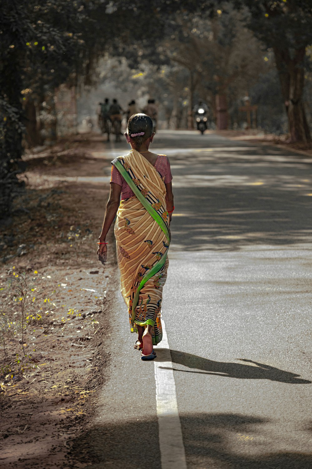 woman in green and brown dress walking on gray asphalt road during daytime