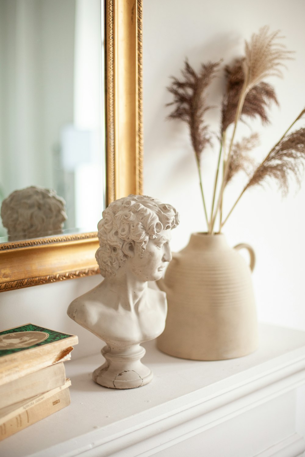 a white vase with a plant in it next to a mirror