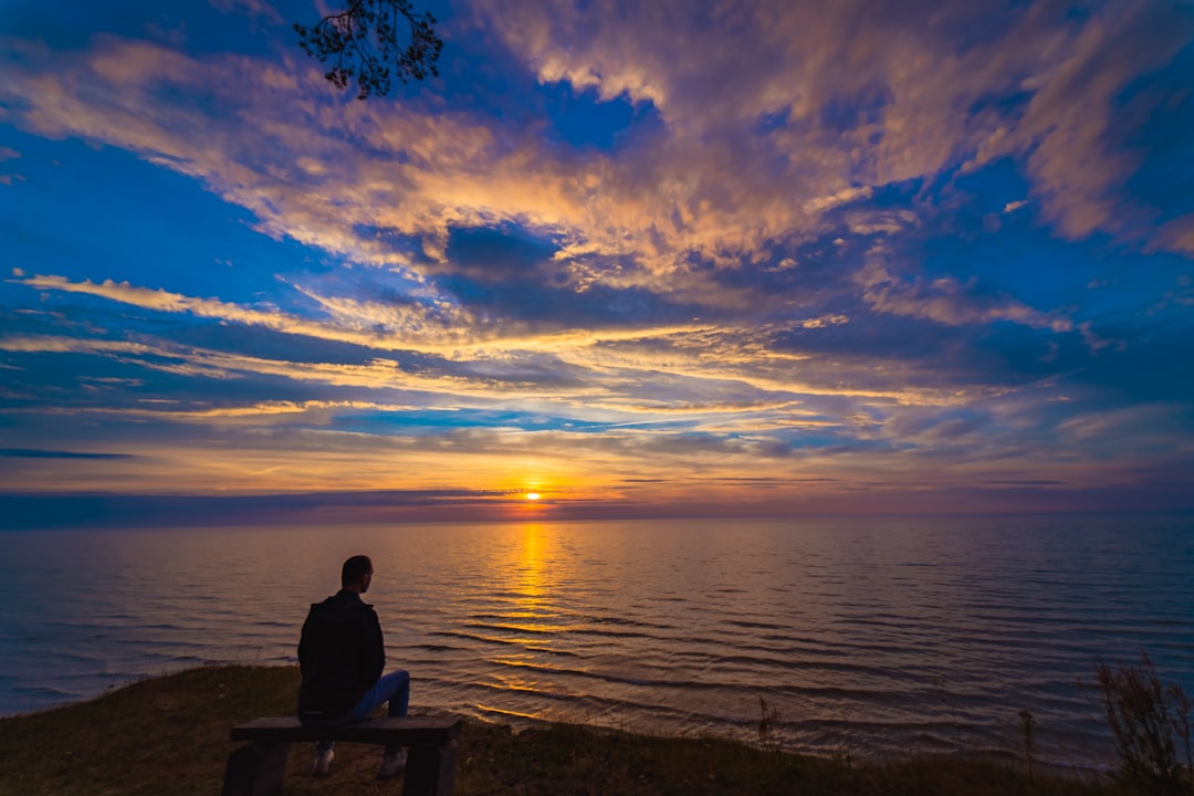 man sitting on bench near sea during sunset