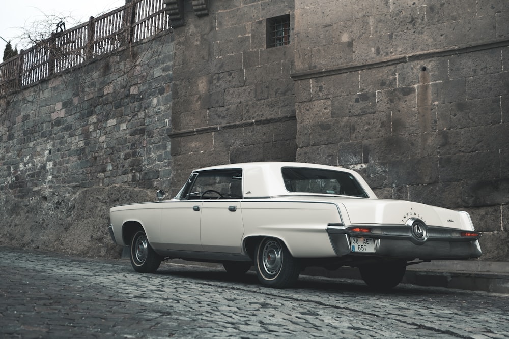 white classic car parked beside brown brick wall