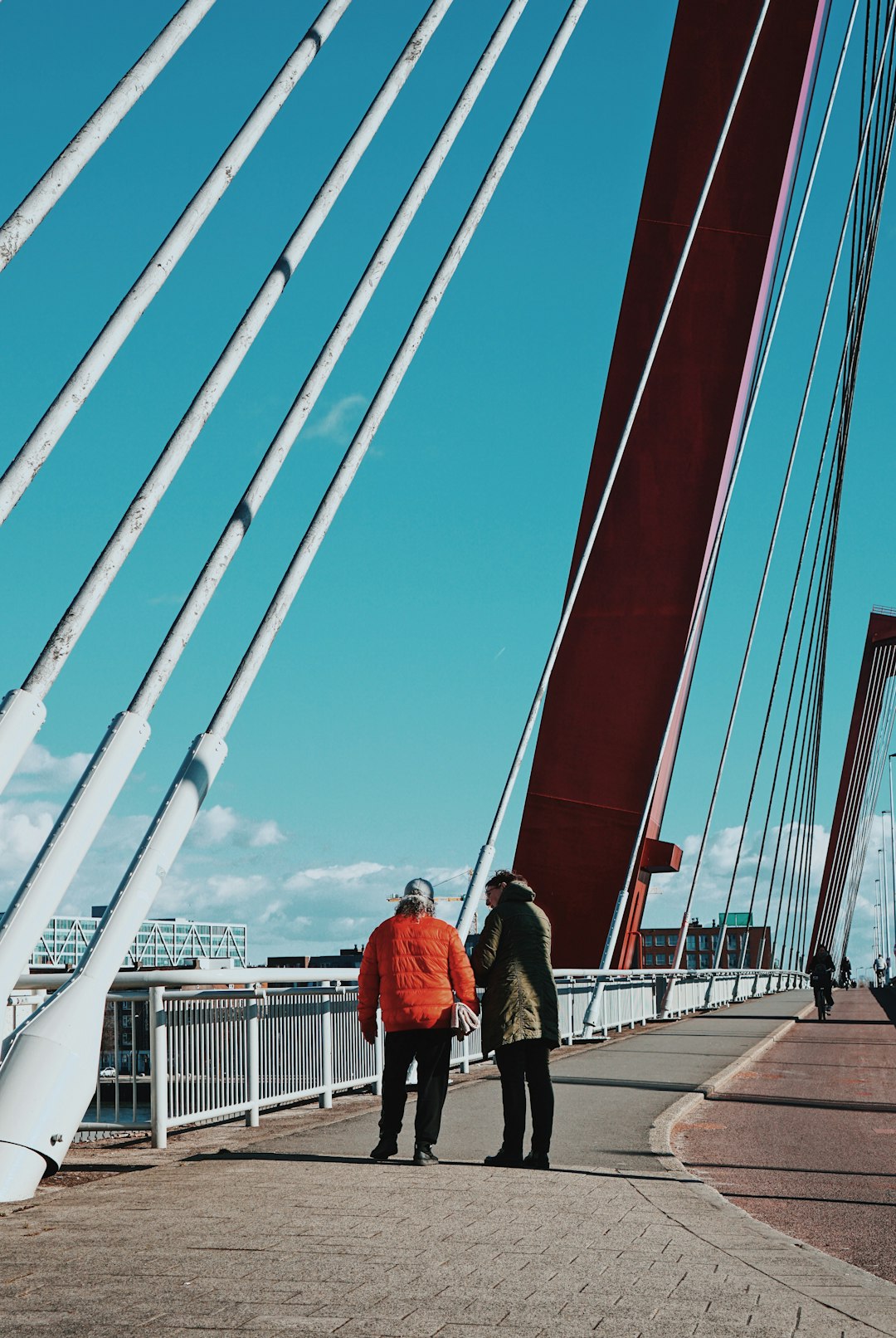 man in red jacket and black pants walking on bridge during daytime