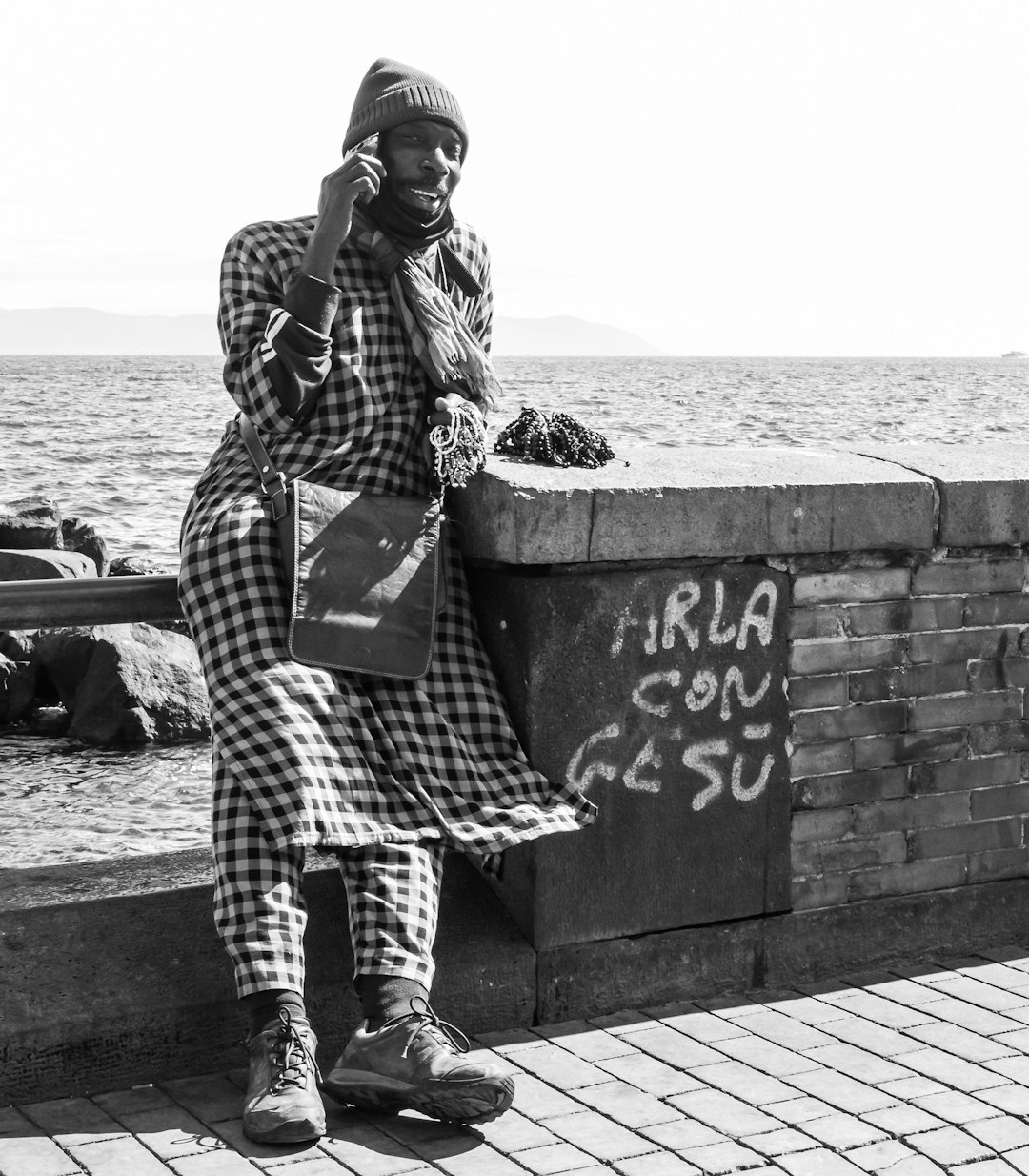 grayscale photo of woman in plaid coat standing on concrete wall near body of water