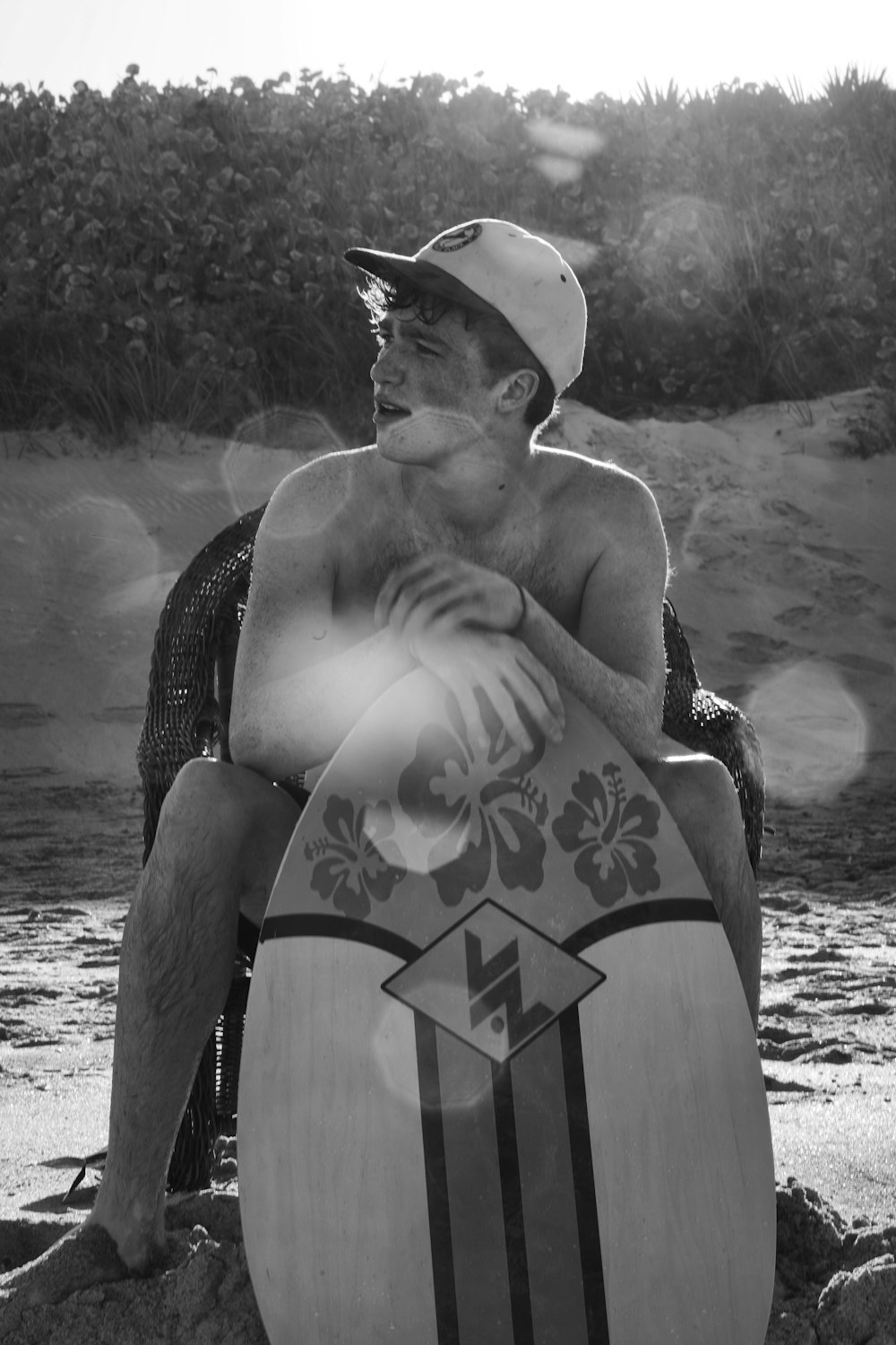 grayscale photo of man wearing hat and holding surfboard