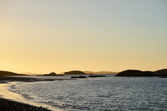 A serene Irish coastline at sunset with rolling green hills meeting the calm blue sea.
