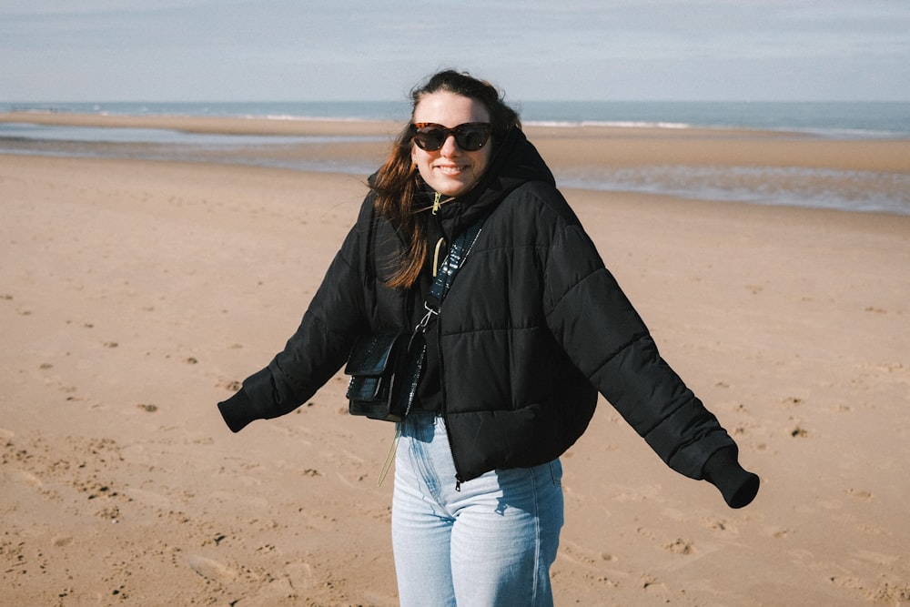 woman in black jacket and blue denim jeans standing on brown sand during daytime