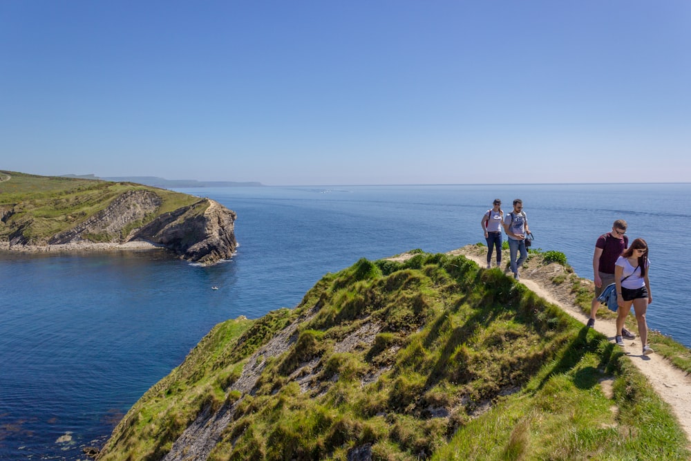 2 people standing on green grass covered hill by the sea during daytime