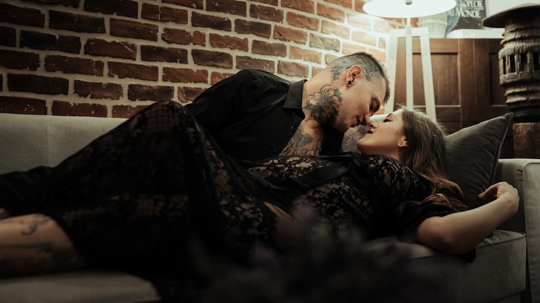 man and woman kissing beside brick wall