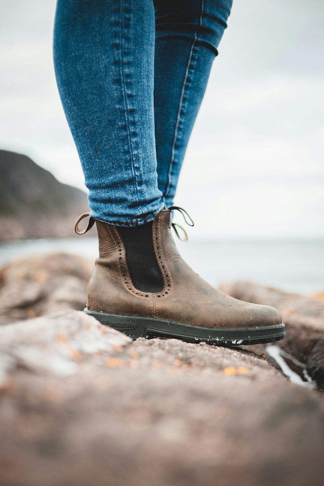 person in blue denim jeans and brown leather boots standing on rocky ground during daytime