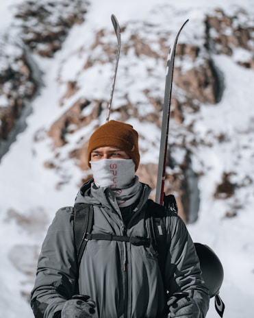 A rugged man wearing a thick, insulated navy blue winter coat standing against a snowy mountain backdrop.