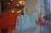 A display of luxury handbags is showcased in a window, featuring vibrant orange, blue, and green tones. The bags have elegant designs, with some resembling confectionery items. The background reflects the interior of a well-lit store with decorative lighting.