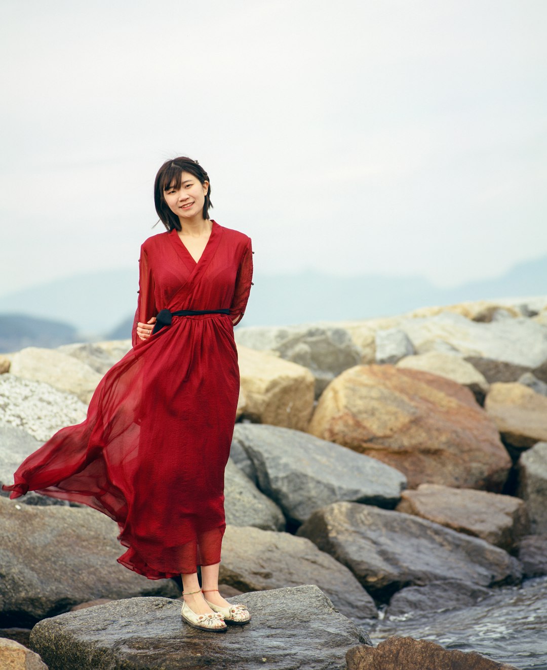 woman in red dress standing on gray rock during daytime