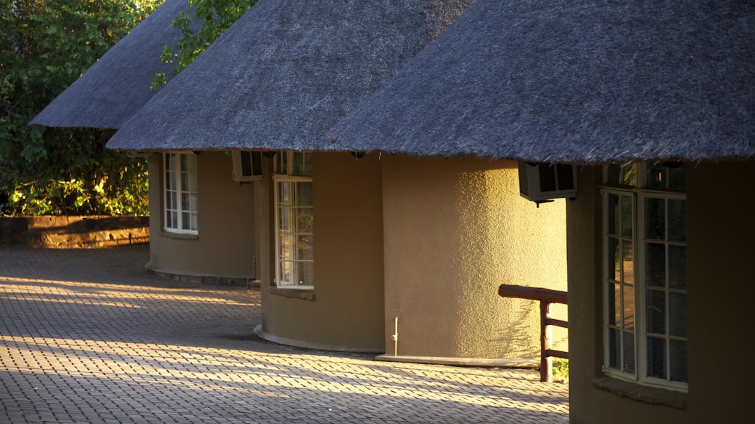 brown wooden bench beside brown concrete house, Late sun on a rondawel<p></figure>