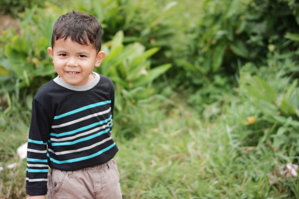 boy in black and white striped shirt standing on green grass field during daytime