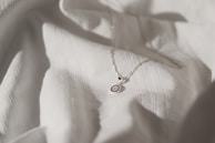 A delicate silver necklace with a small pendant resting on a pastel fabric background.