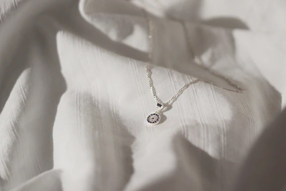 Close-up of a delicate silver necklace pendant with a resin-encased keepsake, softly lit on a blush pink background.