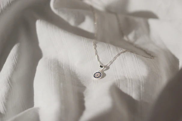 Close-up of a delicate silver necklace with a small sparkling pendant on a soft fabric background