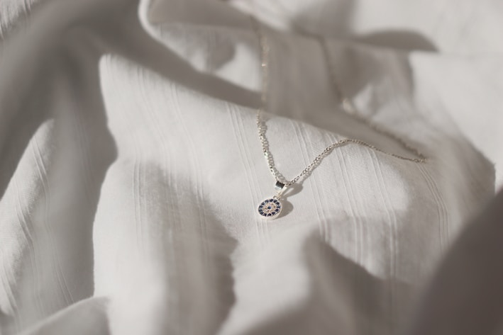 A delicate silver necklace resting on soft fabric, catching gentle light