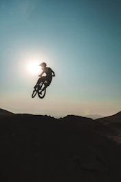 A dynamic shot of a mountain biker mid-air against a sunset backdrop, showcasing energy and motion.