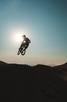 A dynamic photo of a rider leaping their mountain bike off a rugged trail edge at sunset, embodying wild energy and fearless spirit.