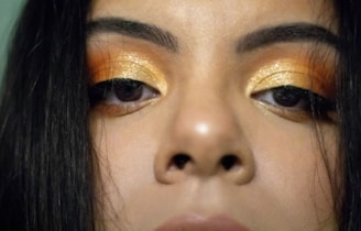 Close-up of a glamorous woman applying gold-toned mascara to her eyelashes, highlighting the luxurious texture.