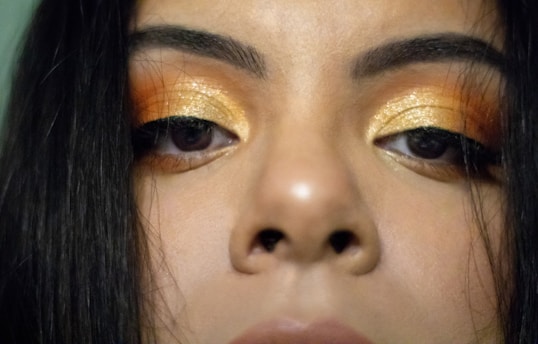 Close-up of a woman’s perfectly shaped, glossy brows with soft champagne gold sparkle accents.
