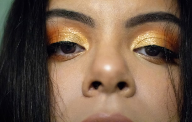 Close-up of a glamorous woman applying gold-toned mascara to her eyelashes, highlighting the luxurious texture.