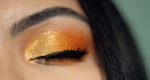 A vibrant eye makeup look with bold, shimmering gold eyeshadow and winged eyeliner.