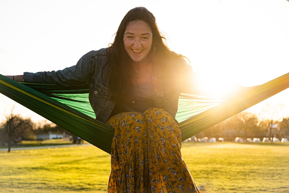 woman in black long sleeve shirt and yellow and green floral dress sitting on green hammock