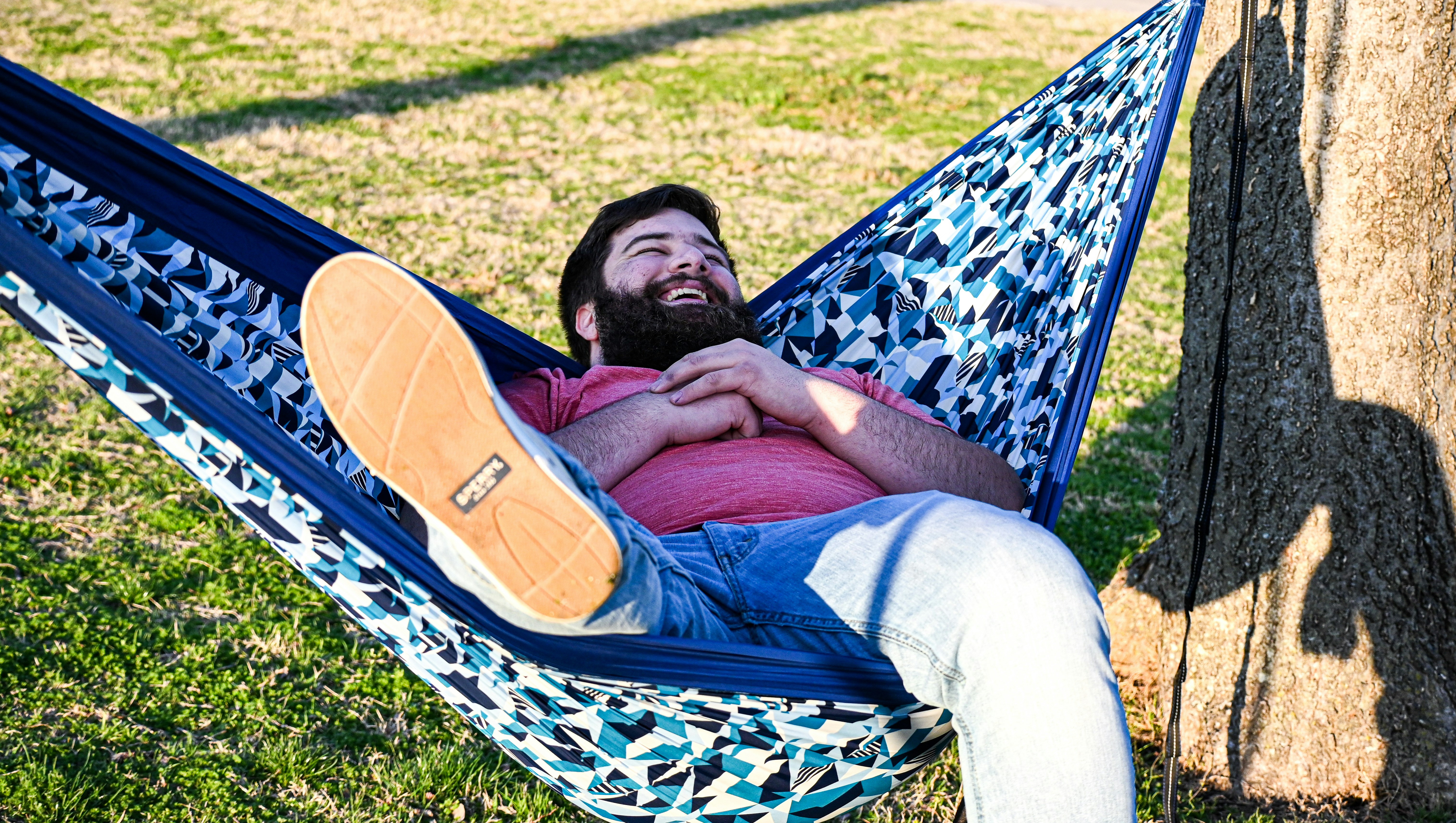 man in red shirt lying on blue and white hammock