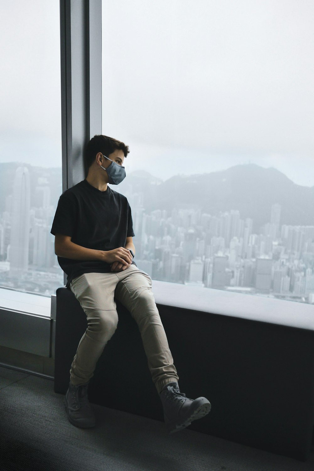 man in black crew neck t-shirt and white pants sitting on window during daytime