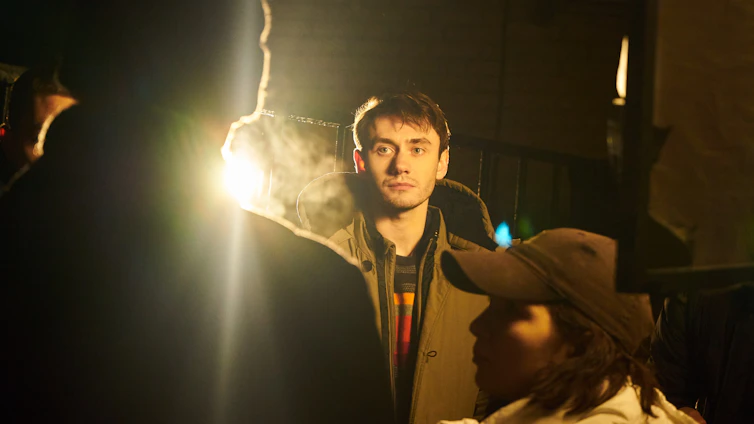 A focused man standing strong against a dark, rugged background with gold light casting a bold silhouette.