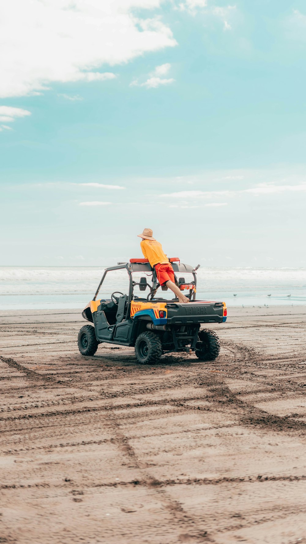 Donna in camicia arancione che si siede su ATV nero e arancione sulla spiaggia durante il giorno